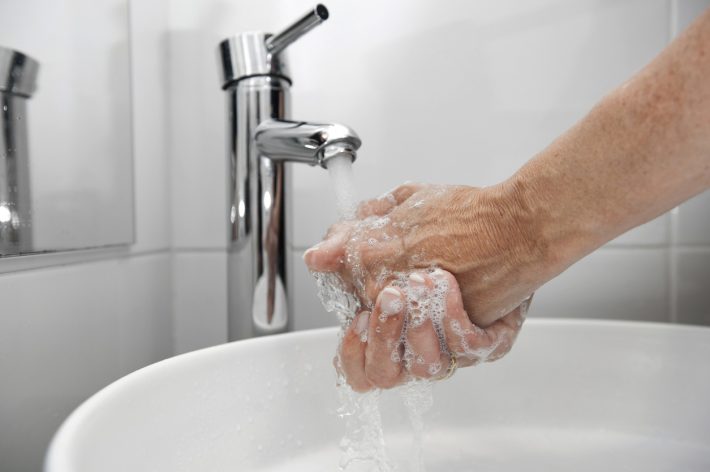 Someone washing their hands in a white sink and a silver tap